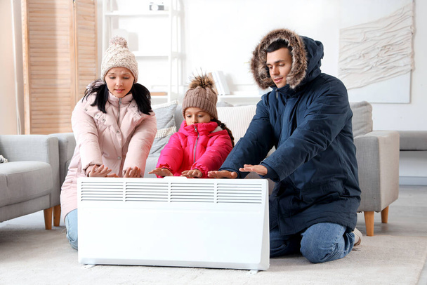 Famille congelée en vêtements d'hiver se réchauffant près du radiateur à la maison - Photo, image