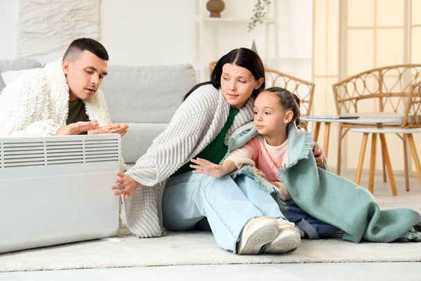 Evde radyatörün yanında ekoseli dondurulmuş bir aile ısınıyor. - Fotoğraf, Görsel