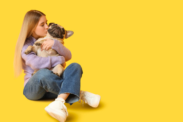 Belle jeune femme embrassant son chien chiot mignon sur fond jaune - Photo, image