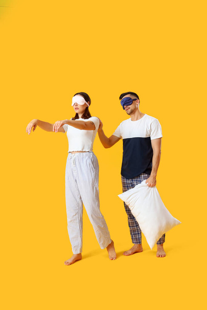 Jeune couple avec des masques de couchage et oreiller sur fond jaune - Photo, image