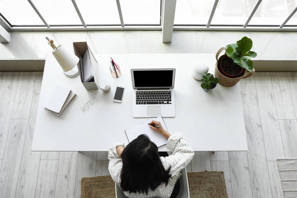 Jonge vrouw werkt met laptop op kantoor, top view - Foto, afbeelding