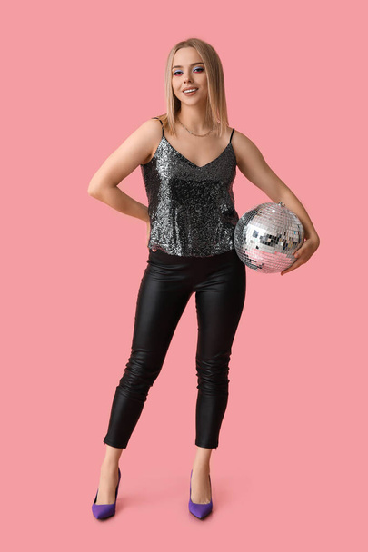 Красива молода жінка з диско-кулькою на рожевому фоні - Фото, зображення
