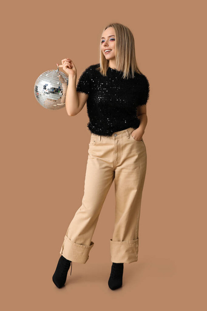 Όμορφη νεαρή γυναίκα με ντίσκο μπάλα σε καφέ φόντο - Φωτογραφία, εικόνα