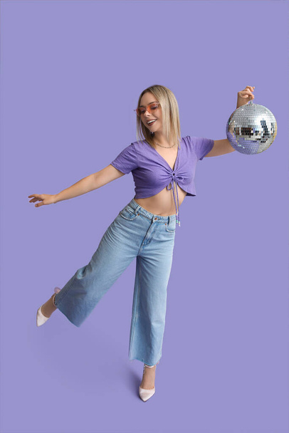 Beautiful young woman with disco ball on purple background - Photo, Image