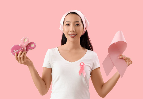 Молодая азиатка с лентой и печеньем на розовом фоне. Концепция информированности о раке груди - Фото, изображение