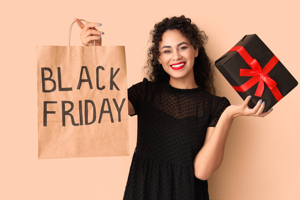 Beautiful African-American woman with gift box and shopping bag on beige background. Black Friday sale - Photo, Image