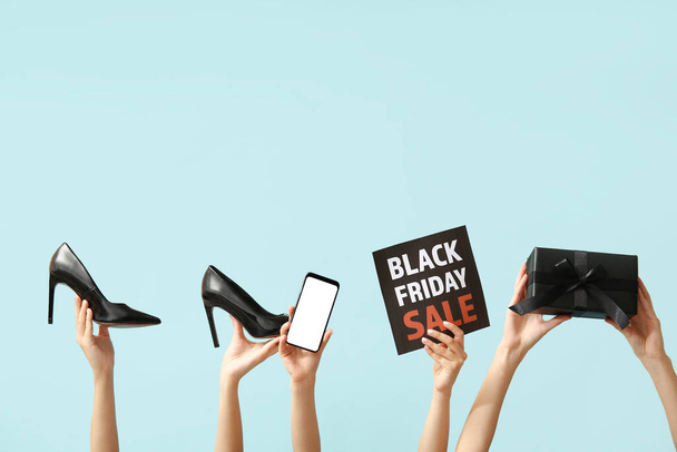 Female hands holding poster with text BLACK FRIDAY SALE, mobile phone, shoes and gift box on blue background - Photo, Image