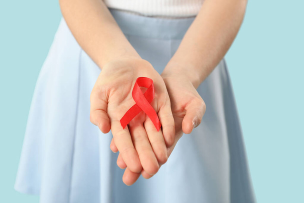 Young woman with red ribbon on blue background, closeup. AIDS concept - Photo, Image