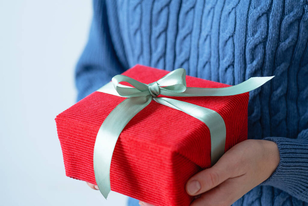 Caja de regalo envuelta en tela roja en manos femeninas. Embalaje ecológico, dar, regalo. Vacaciones sostenibles. Foto de alta calidad - Foto, imagen
