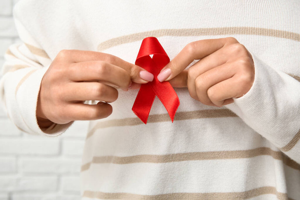 Woman with red ribbon near white brick wall, closeup. World AIDS Day concept - Photo, Image