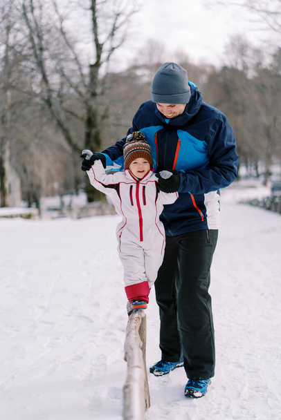 La petite fille marche le long d'une étroite bûche dans le parc, tenant les mains de son père dans un parc enneigé. Photo de haute qualité - Photo, image