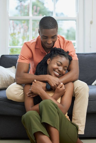 Genç Afro-Amerikan çift evde sarılıyor, kanepede dinleniyorlar. Mutlu, genç bir çiftin evde şefkatle kucaklaşması. Evli çift romantik bir şekilde evde buluşuyor.. - Fotoğraf, Görsel