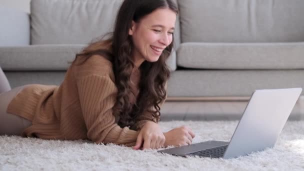 Joyful woman sits on the floor, her face lit up with a genuine smile as she interacts with laptop. The room is filled with a warm, positive energy as she navigates digital tasks with enthusiasm. - Footage, Video