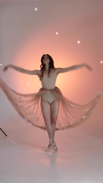Una mujer joven, una bailarina bailando, posa en un estudio de fotografía en una sesión de fotos, moviendo suavemente sus brazos y dedos sobre un fondo rosa, lento, medio. Señora de cabello castaño mujer con el pelo largo - Metraje, vídeo