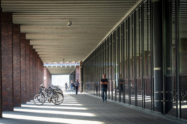 Eine Frau geht in die Ferne, entlang eines modernen Geschäftshauses in Köln. Die Säulen des Gebäudes werfen einen Schatten von der Sonne - Foto, Bild