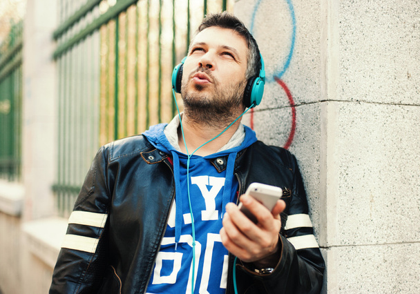 Młody człowiek z słuchawkami grając z inteligentny telefon - Zdjęcie, obraz