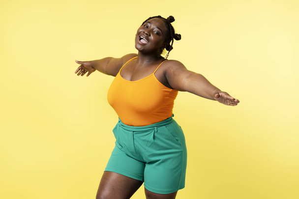 Beautiful attractive plus size African woman wearing casual clothes dancing isolated on yellow background. Body positive female relaxing having fun. Positive lifestyle - Фото, изображение
