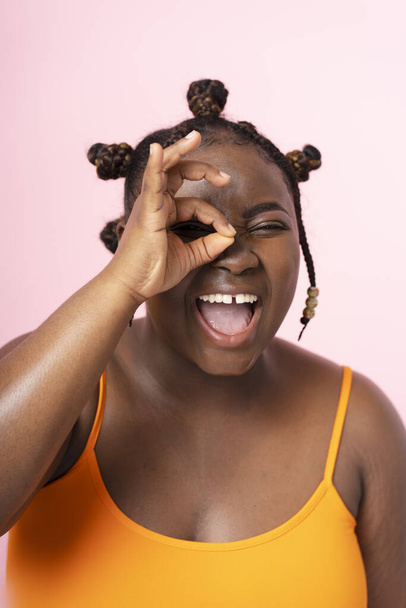 Portré boldog mosolygós nigériai nő gesztikuláló mutató rendben gesztus, megható arc elszigetelt rózsaszín háttér. Pozitív plusz méret nő pózol a kép, közelkép - Fotó, kép