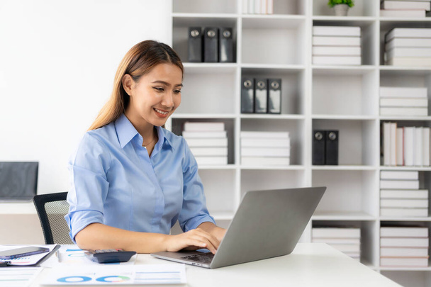 Vidám üzletasszony laptoppal dolgozik, női irodai dolgozó bájosan mosolyog. Együttműködés a pénzügyi dokumentumokkal a vállalati pénzügyi adatok elemzésében. - Fotó, kép