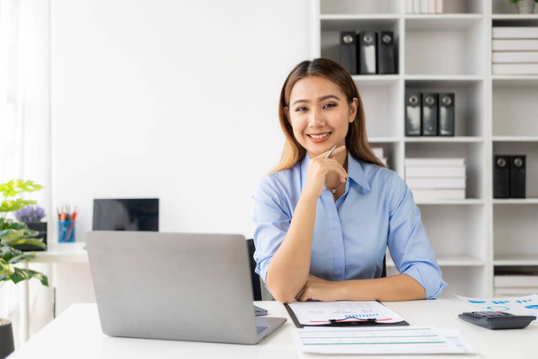 Wesoła bizneswoman pracująca z laptopem, pracownica biurowa uśmiechająca się uroczo. Praca z dokumentami finansowymi w celu analizy danych finansowych firmy. - Zdjęcie, obraz