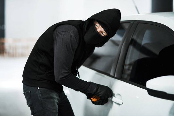 I think I heard someone coming. a masked criminal picking the lock of a car door inside a parking lot - Photo, Image