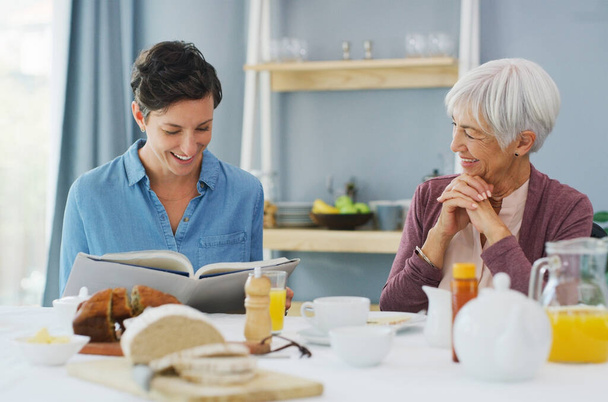 Να δοκιμάσουμε αυτή τη συνταγή μετά. μια ευτυχισμένη ηλικιωμένη γυναίκα που κάθεται και τρώει πρωινό με την ελκυστική νεαρή κόρη της ενώ είναι στο σπίτι - Φωτογραφία, εικόνα