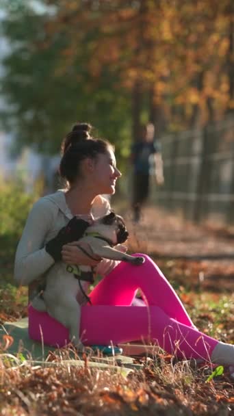 A sárga őszi levelek közepette egy fiatal nő és a mopszlija játékos pillanatokat élnek át a parkban. Kiváló minőségű 4k felvételek - Felvétel, videó