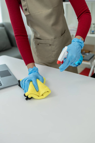 Superficie del escritorio de limpieza en la oficina con aerosol desinfectante, use guantes y limpie la mesa con una toalla, la ama de llaves está limpiando el escritorio para la higiene debido a la Covid-19, idea de limpieza. - Foto, Imagen
