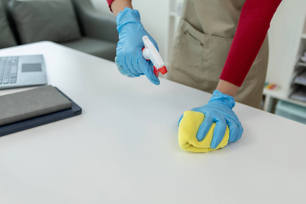 Tisztító asztal felülete az irodában fertőtlenítő spray, viseljen kesztyűt, és törölje le az asztalt egy törülközővel, a házvezetőnő takarítja a munkaasztal higiéniai, mert a Covid-19, tisztítási ötlet. - Fotó, kép