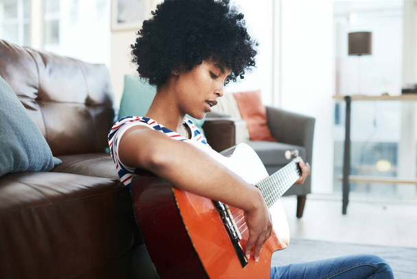 Yeni bir hobi buldum. Genç bir kadın evde otururken gitar çalıyor. - Fotoğraf, Görsel