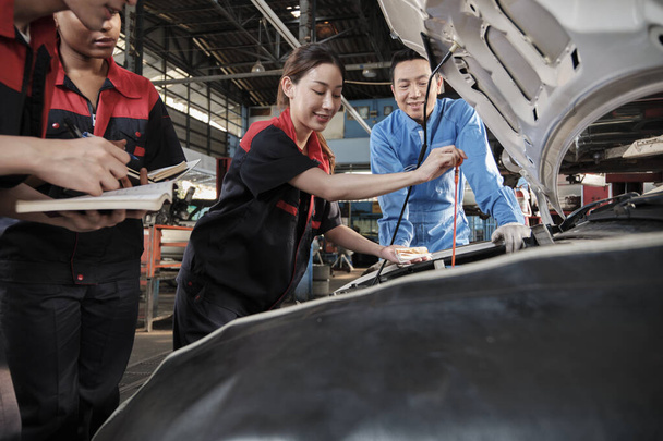 Азиатский профессиональный автомобильный супервайзер консультирует и инспектирует работницу-механика по вопросам жидкого моторного масла в гараже, сервисного обслуживания и ремонта автомобилей.. - Фото, изображение