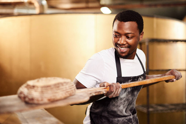Он печет со страстью. мужчина пекарь удаляющий свежеиспеченный хлеб из духовки - Фото, изображение