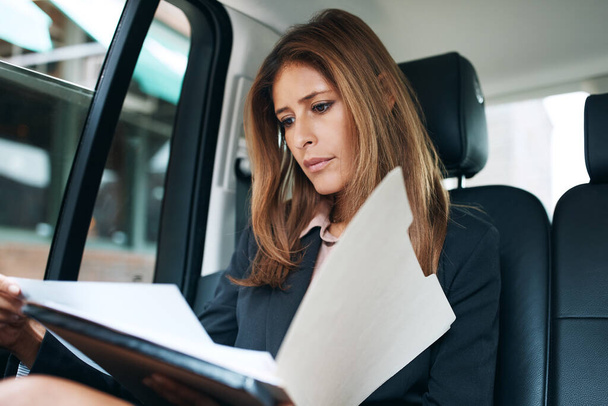 Wer sagte, Arbeit finde nur im Büro statt. eine reife Geschäftsfrau, die auf dem Rücksitz eines Autos Papierkram erledigen muss - Foto, Bild