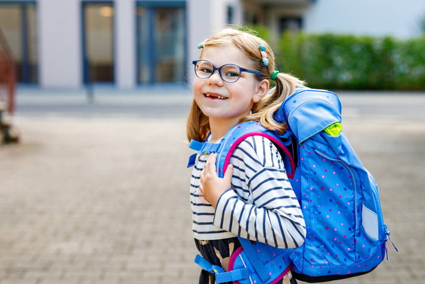 Aranyos kislány az első napján, amikor iskolába megy. Egészséges gyönyörű gyermek sétál óvodába és óvodába. Boldog gyermek szemüveggel hátizsákkal a város utcáján, szabadban - Fotó, kép