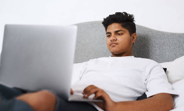Az internet tele van szórakoztatással. egy fiatalember használja a laptopját, miközben fekszik az ágyán. - Fotó, kép