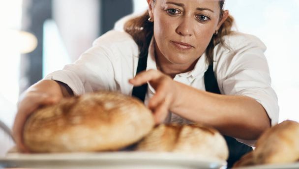Frisch gebackenes Brot kommt gerade recht. eine reife Frau stellt in ihrer Bäckerei eine Auswahl frisch gebackener Brote aus - Foto, Bild