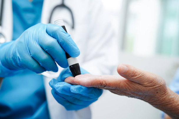 Aziatische arts met lancet pen op senior patiënt vinger voor controle monster bloedsuikerspiegel aan behandeling diabetes - Foto, afbeelding