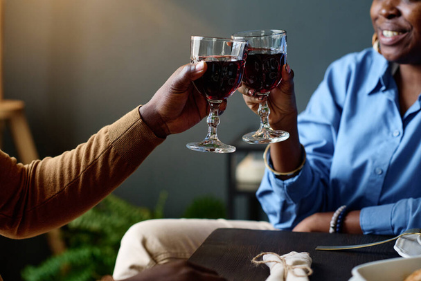 Сосредоточьтесь на руках молодой афроамериканской гетеросексуальной пары, пьющей бокалы, сидя перед камерой за столом в ресторане - Фото, изображение