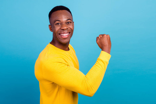 Portrait of strong cheerful man with trendy haircut wear yellow outfit demonstrate biceps clenching fist isolated on blue color background. - Φωτογραφία, εικόνα