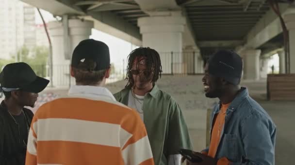 Diverse gang of four talking while standing under city bridge together at daytime - Metraje, vídeo