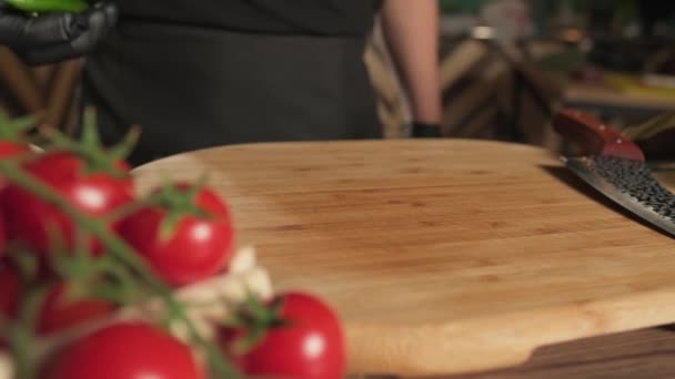 Cuoco in guanti che lancia peperoni sul tagliere accanto a pomodori, erbe e verdure. Rallentare, Avvicinare. - Filmati, video