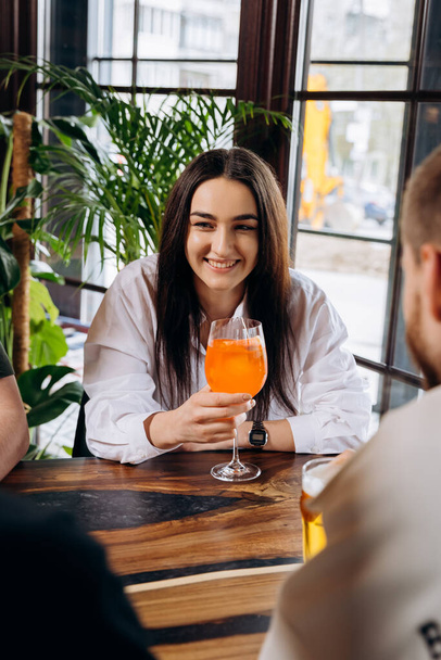 Молодая улыбающаяся женщина, наслаждающаяся коктейлем в баре ресторана во время отдыха с друзьями - Фото, изображение