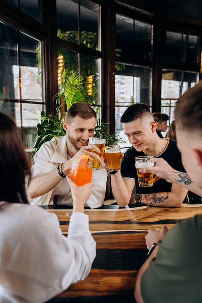 Boldog baráti társaság, akik sörrel és koktélokkal isznak és koccintanak a sörfőzde bárjában. - Fotó, kép