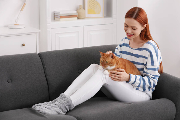 Happy woman with her cute cat on sofa at home - Фото, изображение