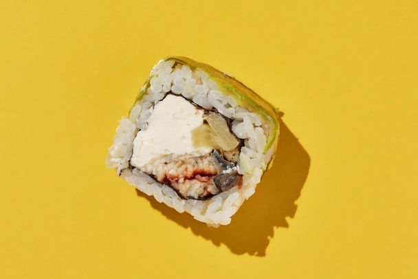 Свежий суши-ролл с угрем, ананасом, сыром и авокадо на желтом фоне, вид сверху. - Фото, изображение