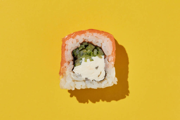 Свежий суши ролл Филадельфия с лосося, сыра и огурца на желтом фоне, вид сверху. - Фото, изображение
