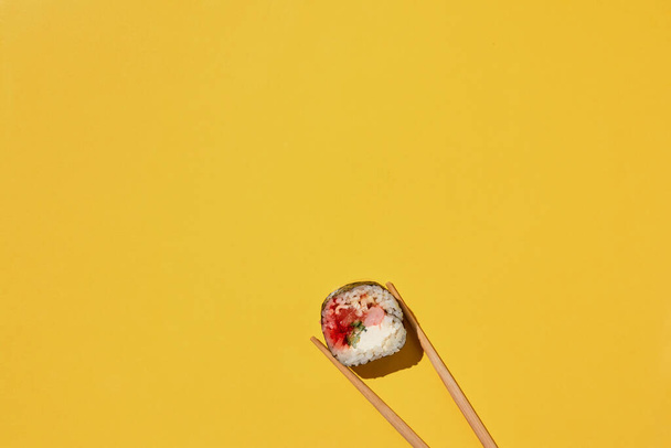 Rouleau de sushi maki frais avec crevettes, anguille, saumon, fromage et cucucmber et baguettes sur fond jaune, vue de dessus. - Photo, image