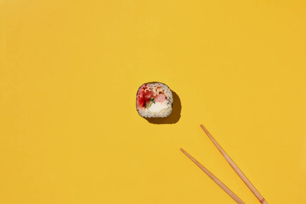 Čerstvé maki sushi rolka s krevetami, úhořem, lososem, sýrem a okurkou a hůlkami na žlutém pozadí, horní pohled. - Fotografie, Obrázek