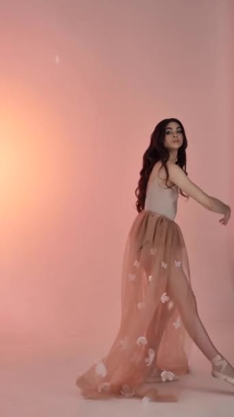 Une jeune femme, une danseuse de ballerine, pose dans un studio photo lors d'une séance photo, bougeant doucement ses bras et ses doigts sur un fond rose, ralenti, moyen. Dame aux cheveux bruns avec les cheveux longs - Séquence, vidéo
