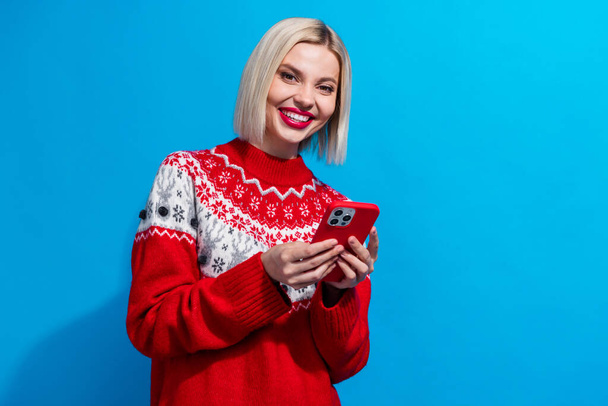 Portrét atraktivní pozitivní dívka zubatý úsměv držet chytrý telefon prázdný prostor reklama izolované na modrém pozadí. - Fotografie, Obrázek
